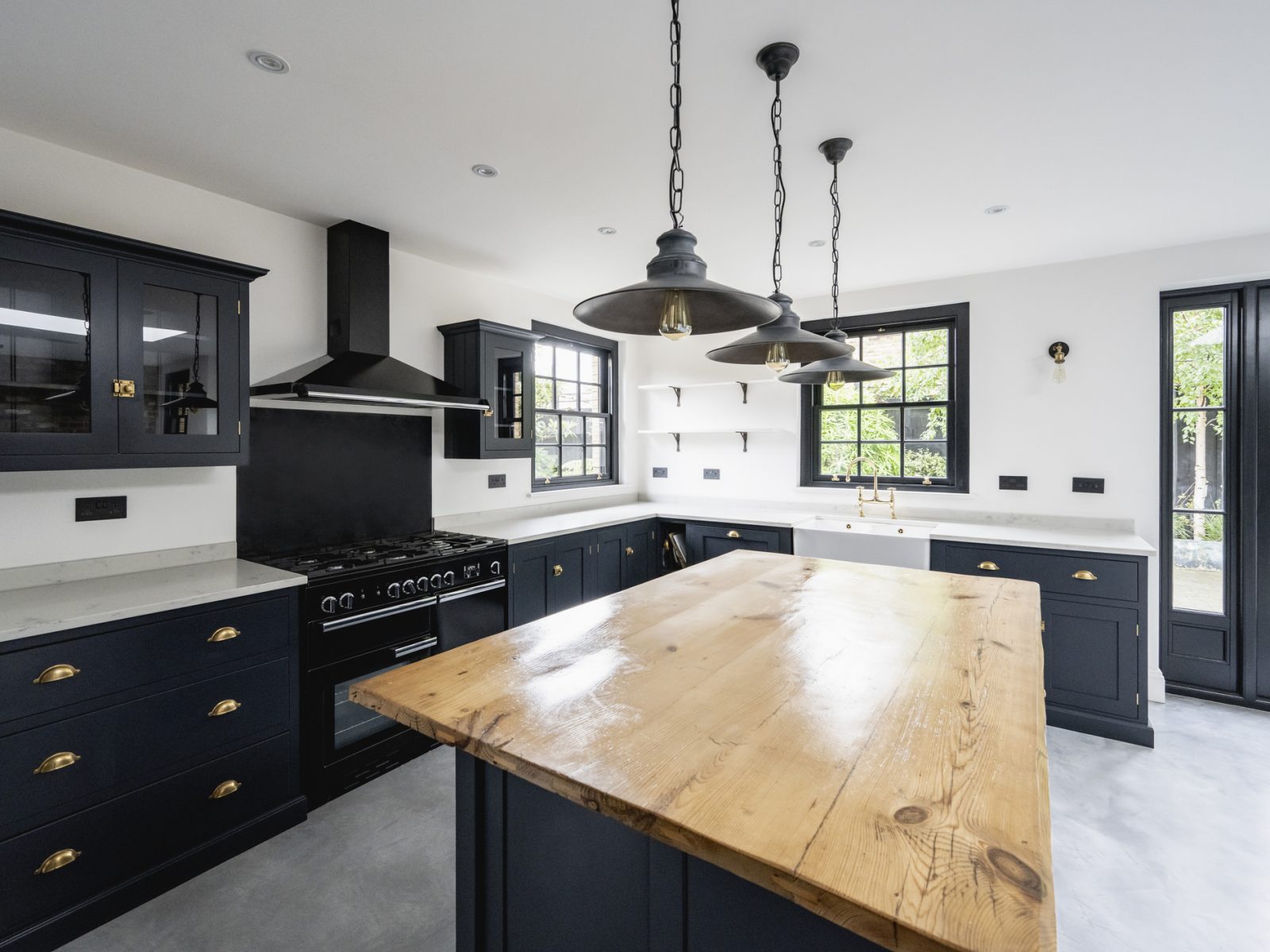 Expansive view of granite countertops, kitchen island, pendant lights, black accented cabinets and appliances, and access to outdoor patio.