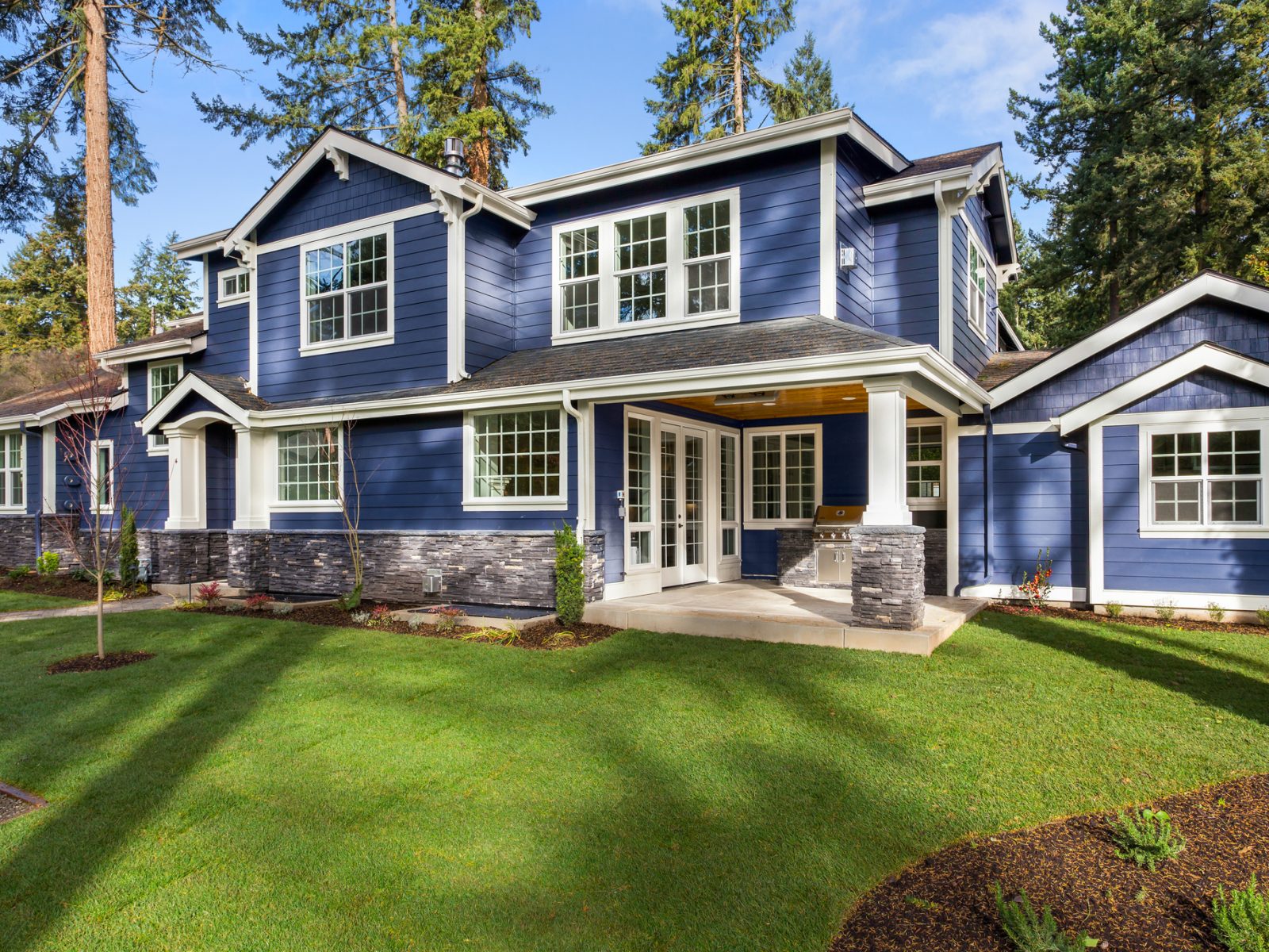 facade of home with manicured lawn, and backdrop of trees and blue sky